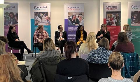 Panel of women in discussion in front of a seated crowd 